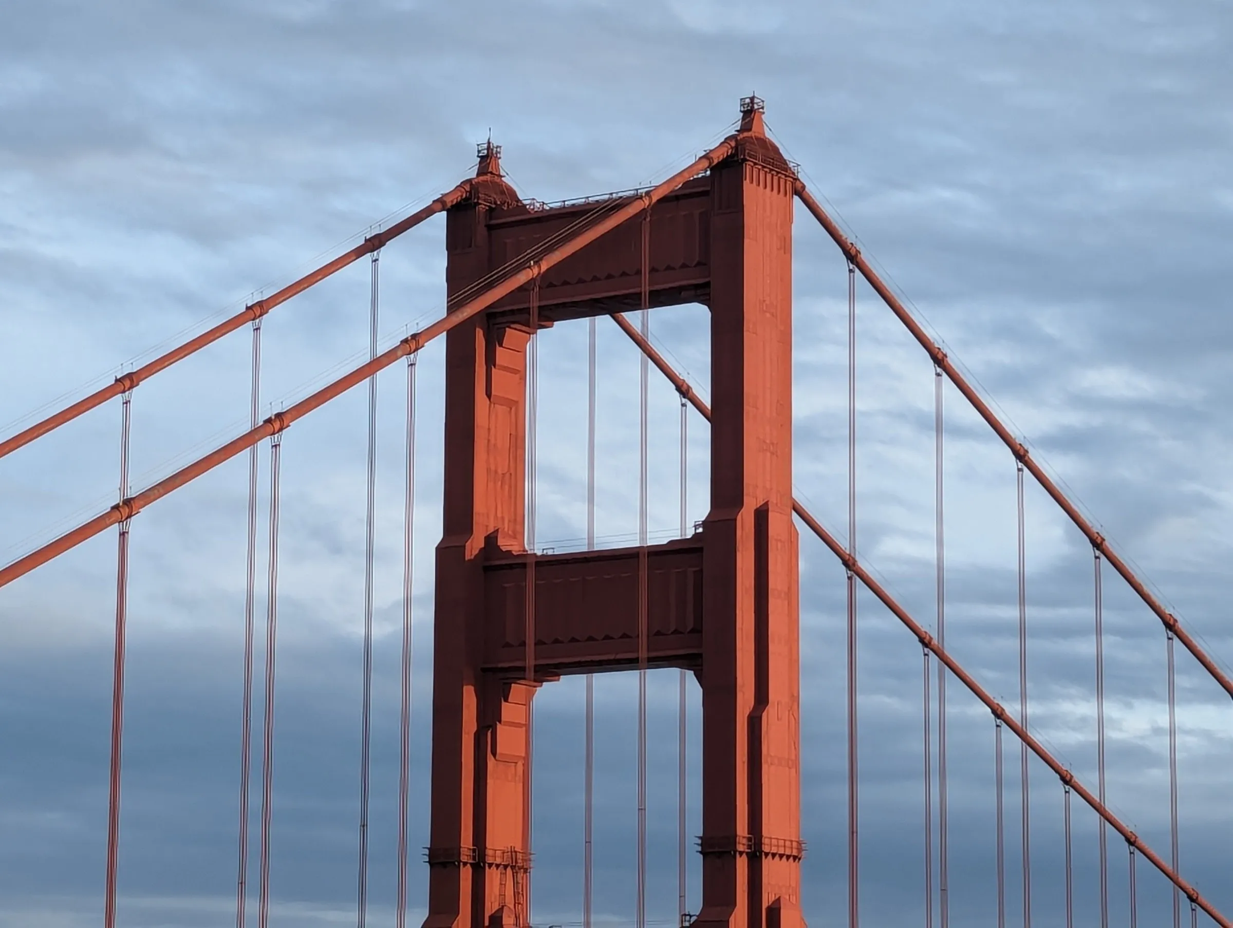 Golden Gate Bridge tower in warm orange light against blue sky with suspension cables