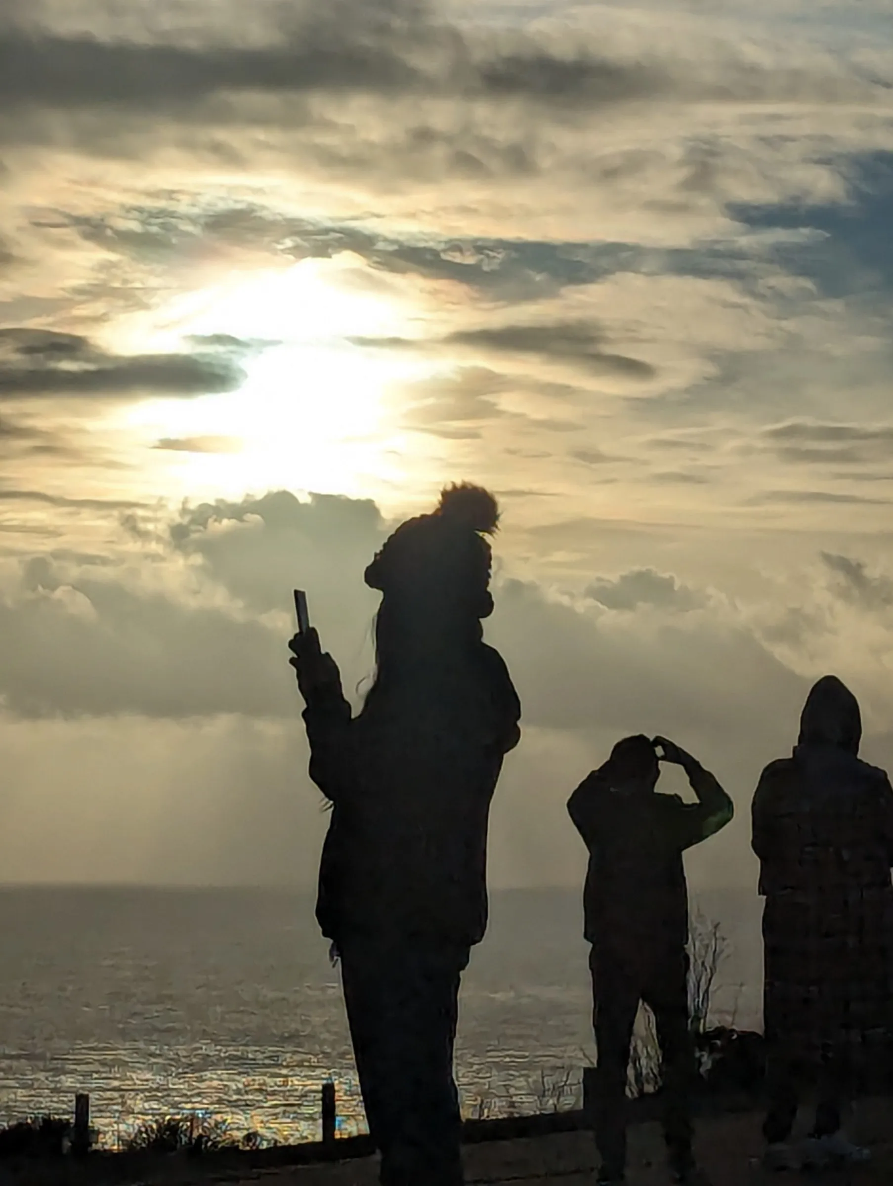 Silhouettes of three people watching sunset over ocean with dramatic cloud formations
