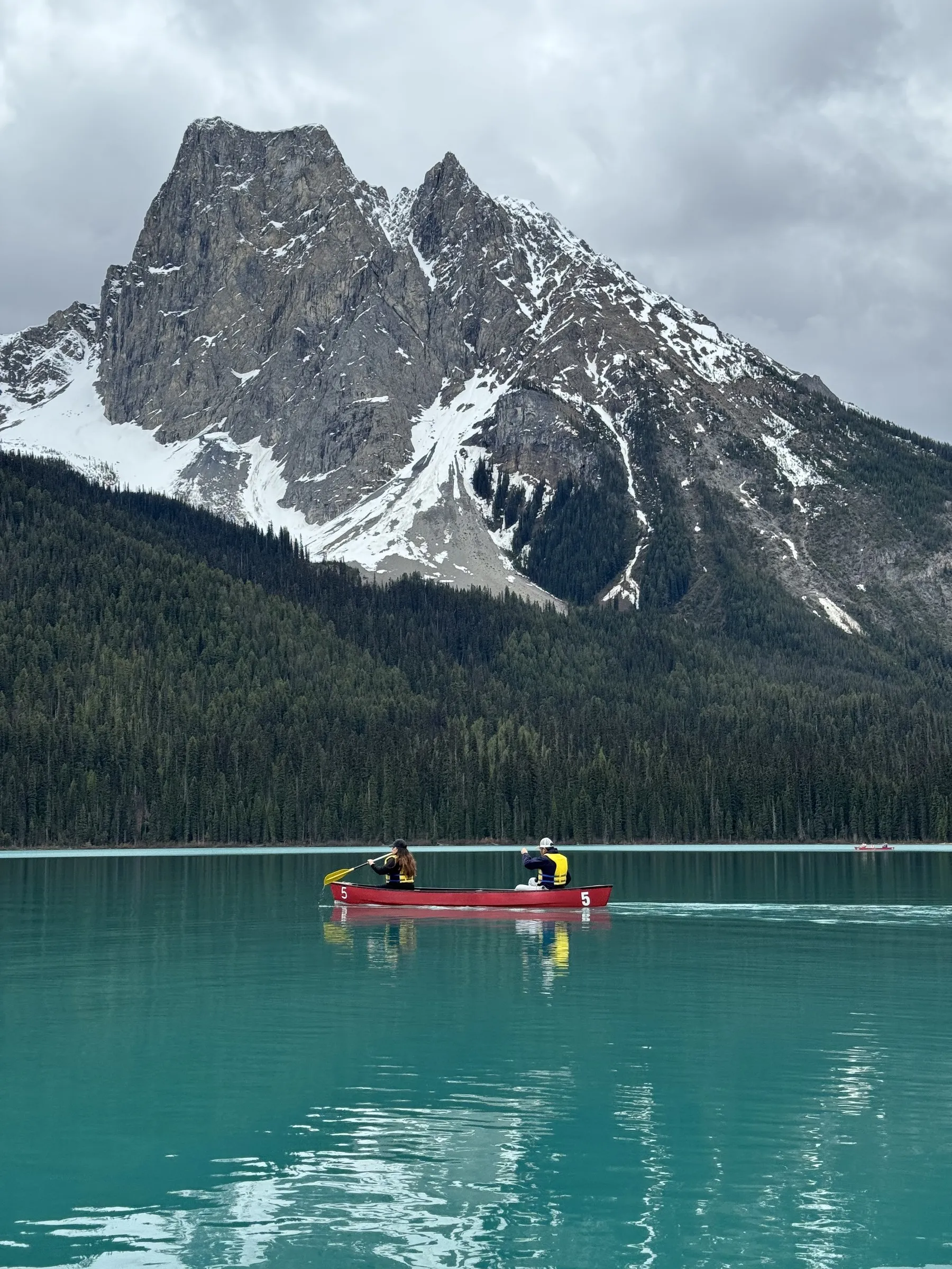 Two people in red canoe on turquoise alpine lake with snow-capped mountain peak behind