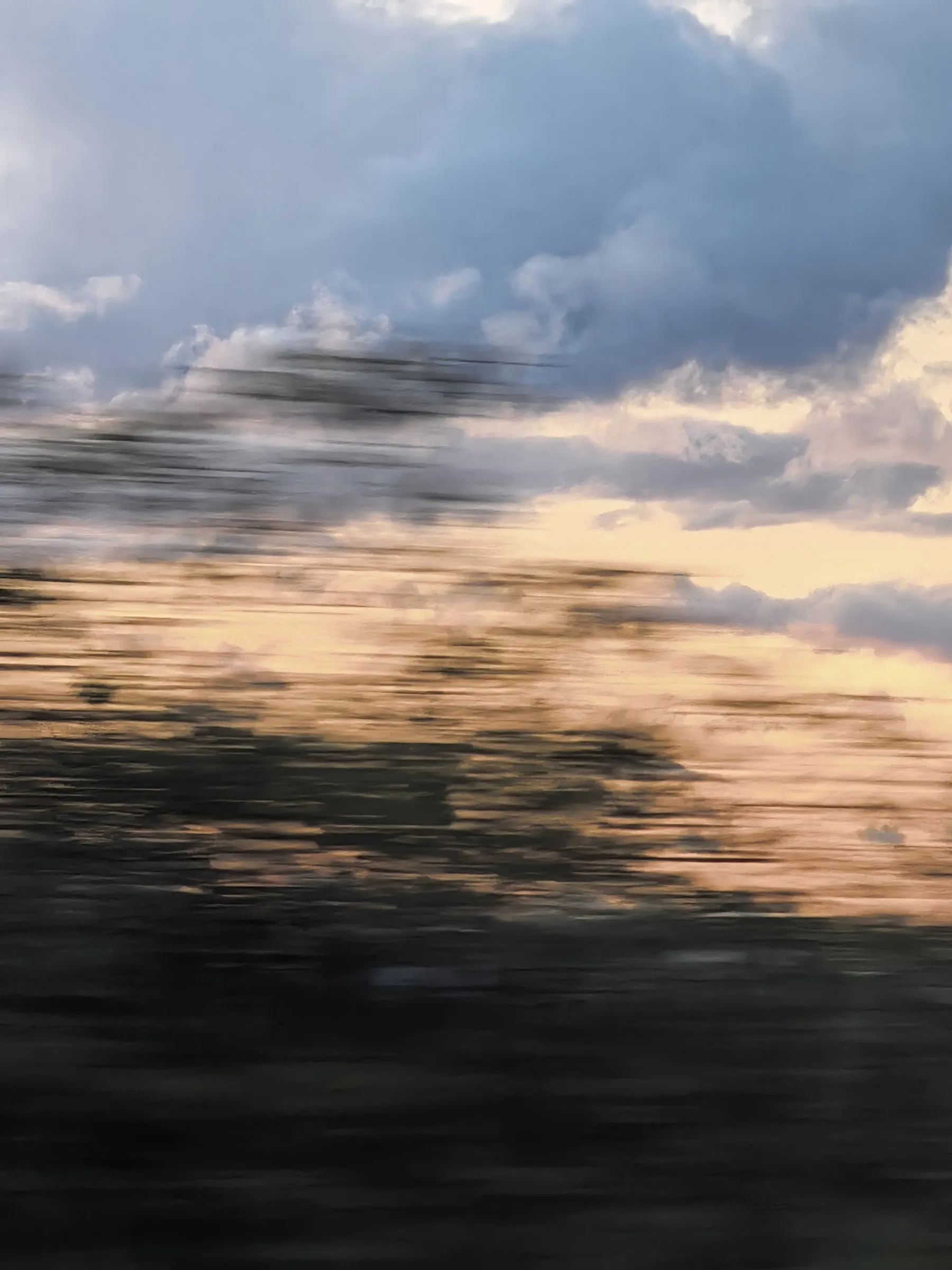 Motion-blurred view from moving train showing landscape with cloudy sky rendered as horizontal streaks.